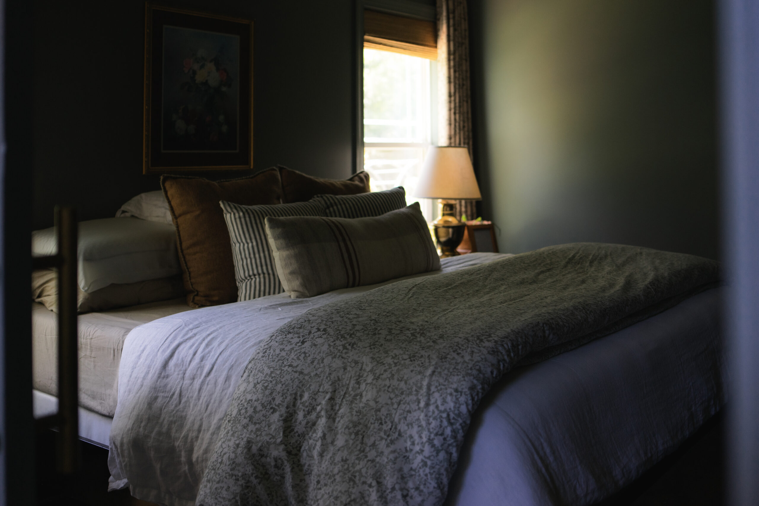 Moody bedroom featuring vintage-inspired bedding, warm lighting, and a mix of classic prints for a layered, old-world feel.
