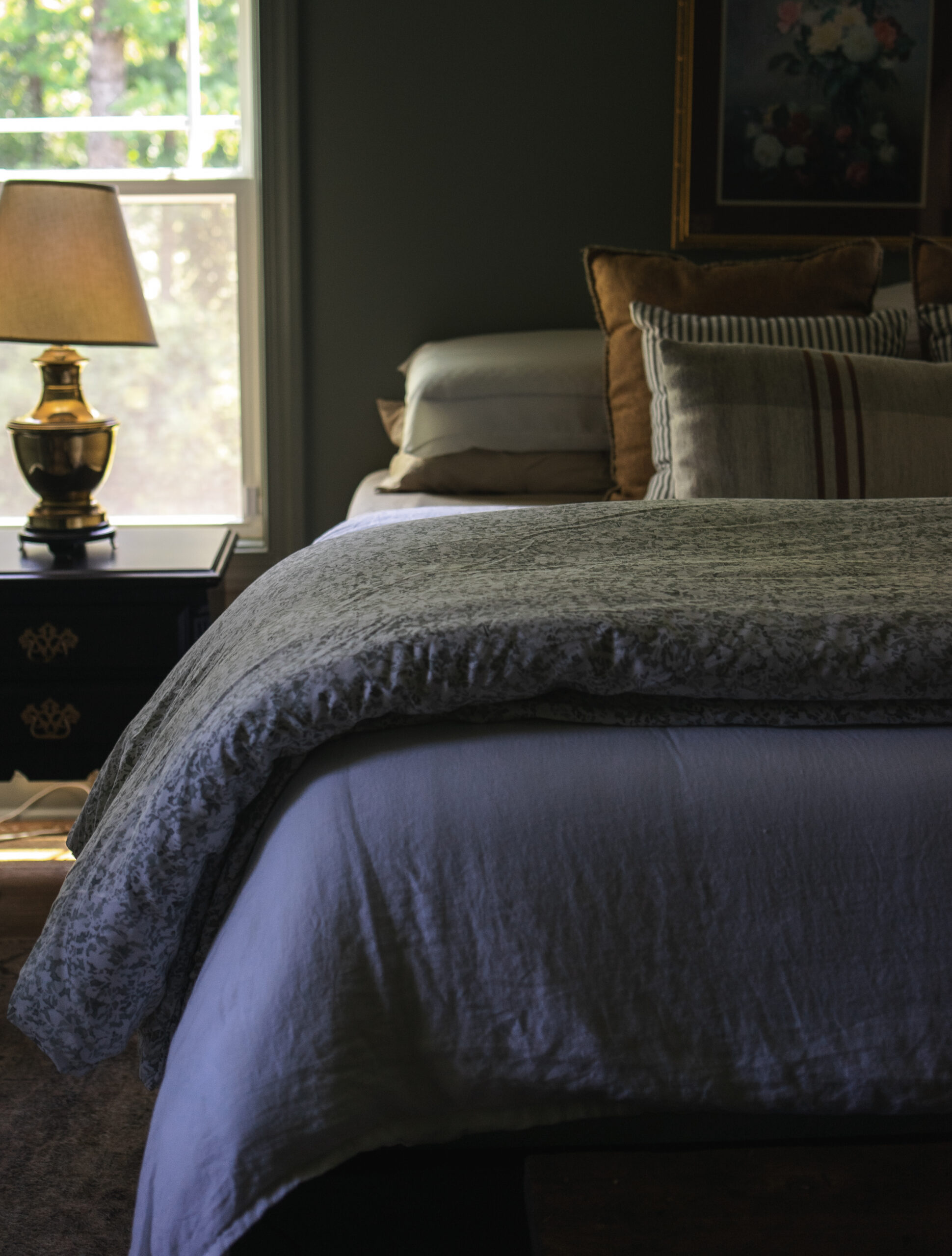 Vintage floral comforter layered on a moody-toned bed with dark green walls and patterned curtains, creating a cozy and timeless bedroom look.