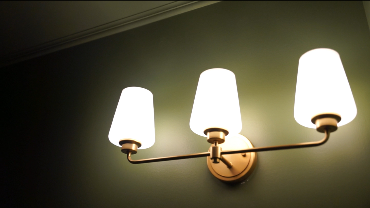 ewly installed brushed gold vanity light with three clear glass shades mounted above a bathroom mirror, casting warm, even light across the vanity area
